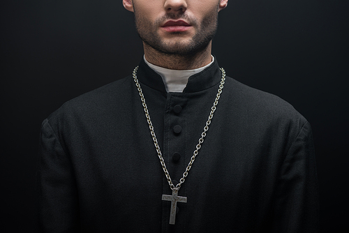 partial view of catholic priest with silver cross on necklace isolated on black