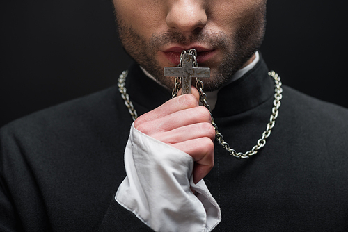 cropped view of catholic priest kissing silver cross on his necklace isolated on black