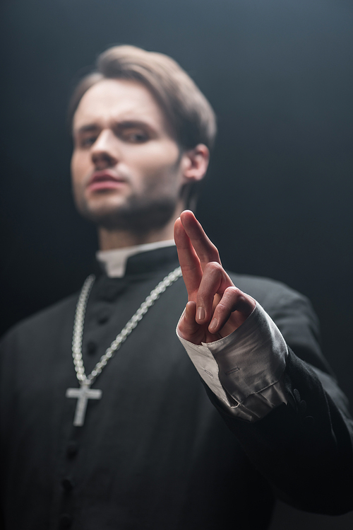 low angle view of confident catholic priest showing blessing gesture isolated on black