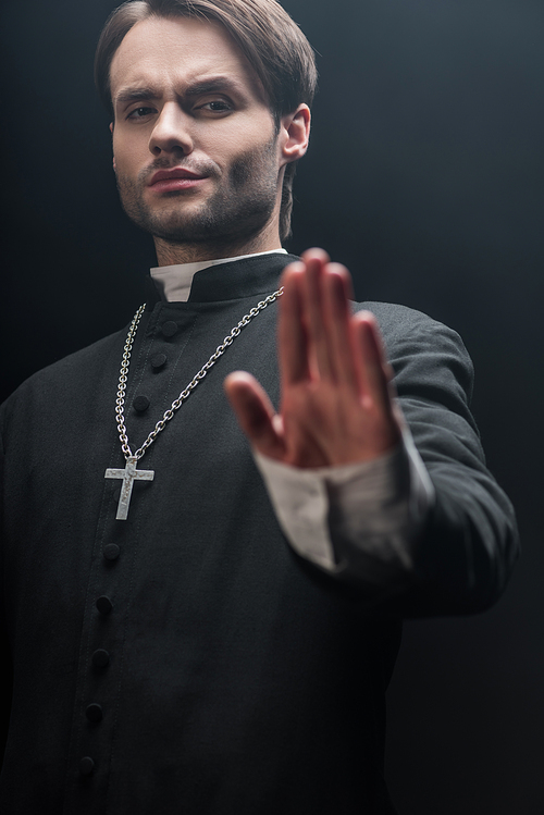 low angle view of strict catholic priest showing refuse gesture isolated on black