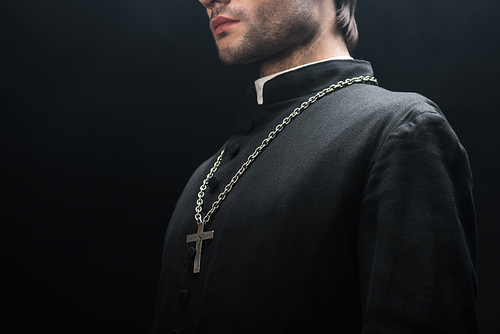 cropped view of catholic priest in black cassock with silver cross on necklace isolated on black
