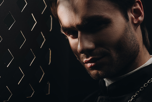 portrait of young tense catholic priest  near confessional grille in dark with rays of light