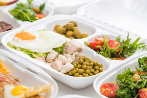selective focus of  package with vegetables, meat, fried egg and salad on white background