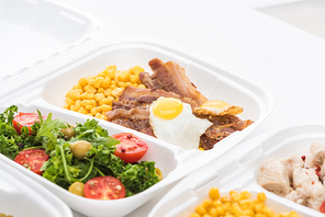 selective focus of  package with corn, meat, fried egg and salad on white background