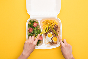 cropped view of woman eating from  package with corn, meat, fried eggs and salad isolated on yellow