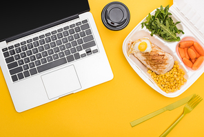 top view of paper cup, laptop and  package with vegetables, meat, fried egg and arugula isolated on yellow