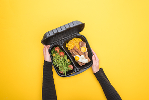 cropped view of woman holding  package with corn, meat, fried eggs and salad isolated on yellow