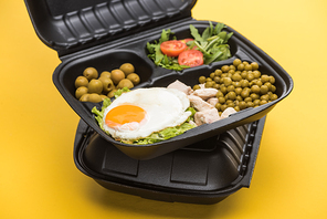 package with vegetables, meat, fried egg and salad isolated on yellow