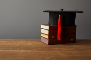 Academic cap and books on wooden surface isolated on grey