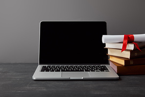 Laptop with blank screen, diploma and books isolated on grey