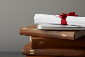 Brown books, laptop and diploma with red ribbon isolated on grey