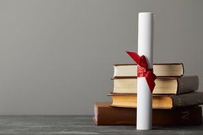 Diploma with red ribbon and books on textured surface isolated on grey