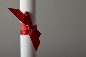 Close up view of diploma with red ribbon isolated on grey