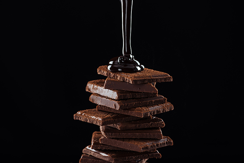 Hot melted dark chocolate pouring on chocolate stack, isolated on black