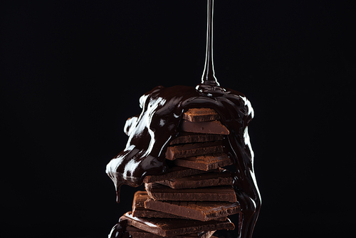 Hot melted chocolate pouring on chocolate stack, isolated on black