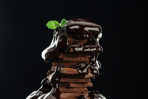 Dark chocolate stack with melted chocolate and fresh mint isolated on black