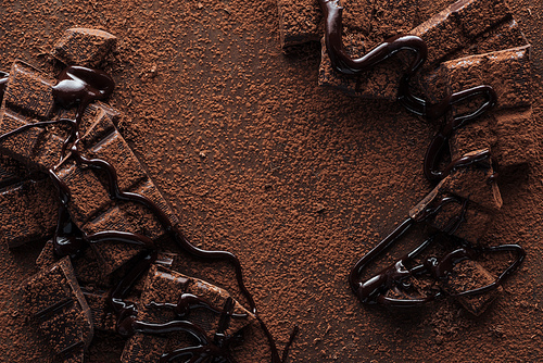 Top view of pieces of chocolate with liquid chocolate and cocoa powder on metal background