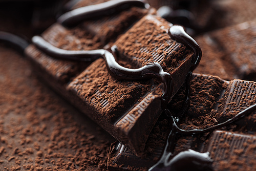 Close up view of pieces of dark chocolate bar with liquid chocolate and cocoa powder