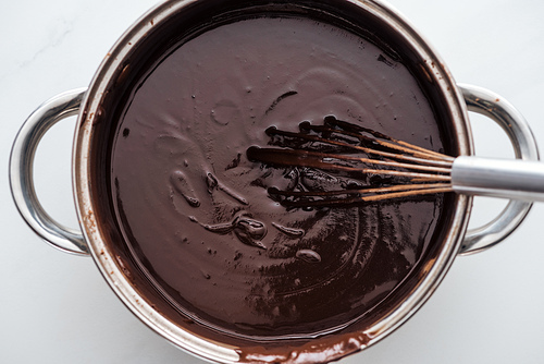 Top view of pan with melted dark chocolate and balloon whisk