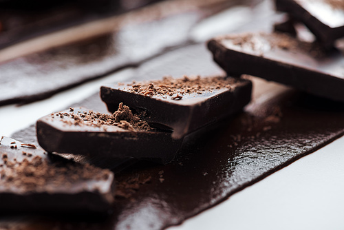 Selective focus of pieces of chocolate bar with cocoa powder and melted chocolate