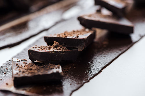Selective focus of pieces of chocolate bar with cocoa powder