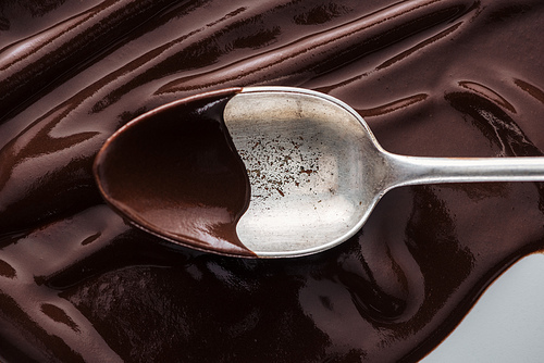 Close up view of vintage spoon covered of chocolate on melted chocolate background