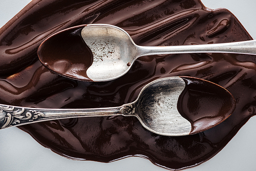 Top view of spoons covered of chocolate and melted chocolate on white background