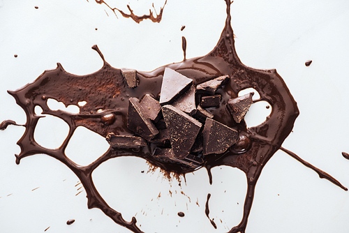 Top view of pieces of dark chocolate with splash of melted chocolate