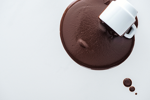 Top view of cup with spilling chocolate and chocolate drops on white background
