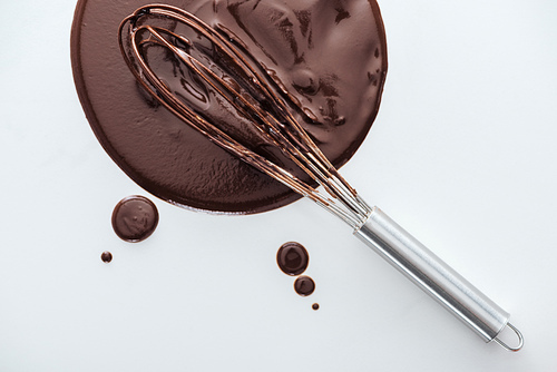 Top view of balloon whisk with circle of melted chocolate on white background