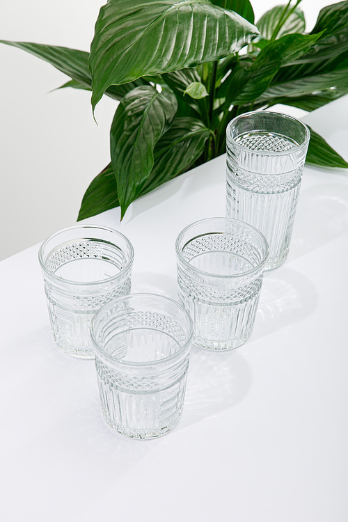 faceted glasses of fresh water on white table near green peace lily plant