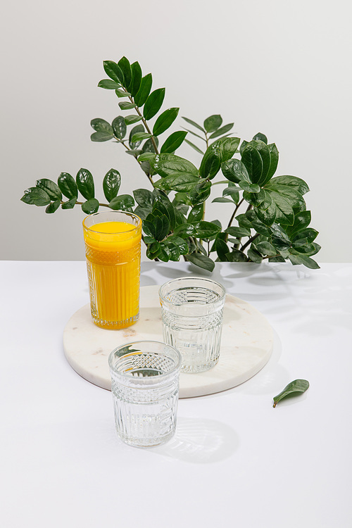 glass of delicious yellow smoothie on white surface near green peace lily plant isolated on grey