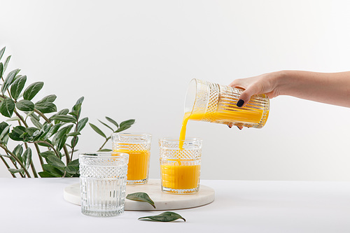 cropped view of woman pouring delicious yellow smoothie in glass on white surface near green plant
