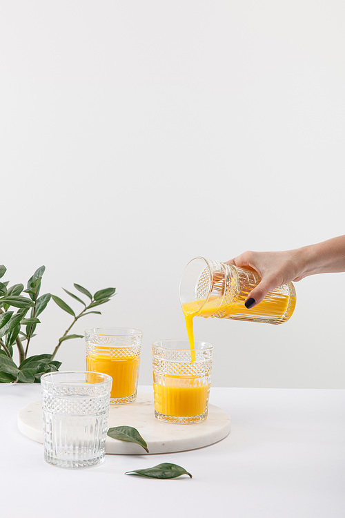 cropped view of woman pouring delicious yellow smoothie in glass near green plant isolated on white