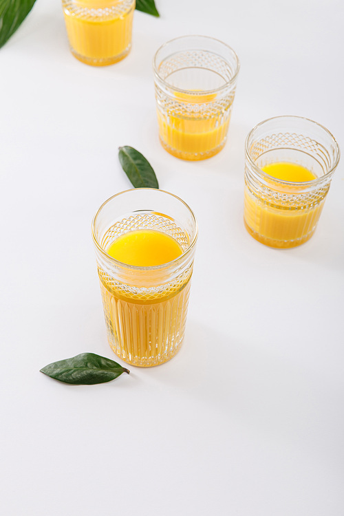 glasses of fresh delicious yellow smoothie on white surface with green leaves