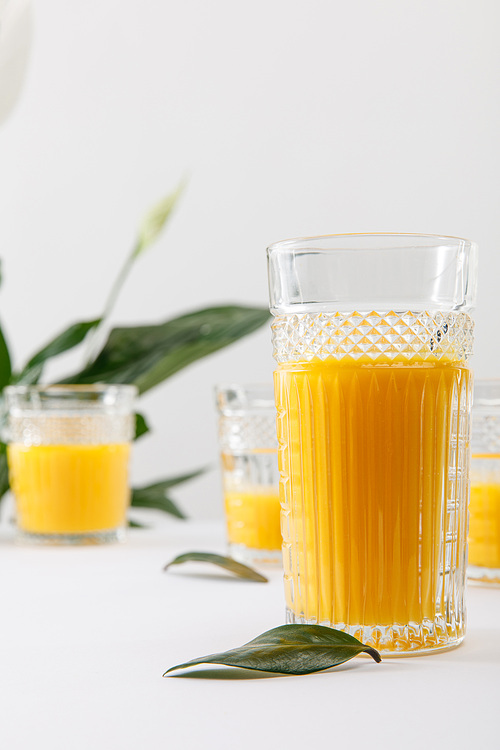 selective focus of glass of fresh delicious yellow smoothie on white surface near green peace lily plant isolated on grey