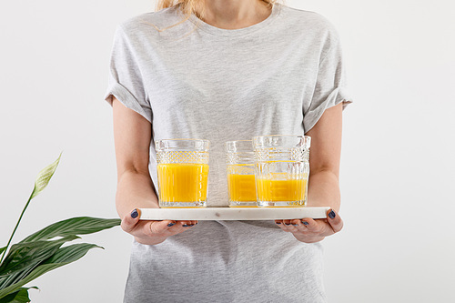 cropped view of woman holding tray with glasses of fresh delicious yellow smoothie near green peace lily plant isolated on white