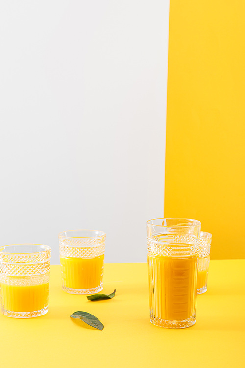 glasses of fresh delicious yellow smoothie near green leaves