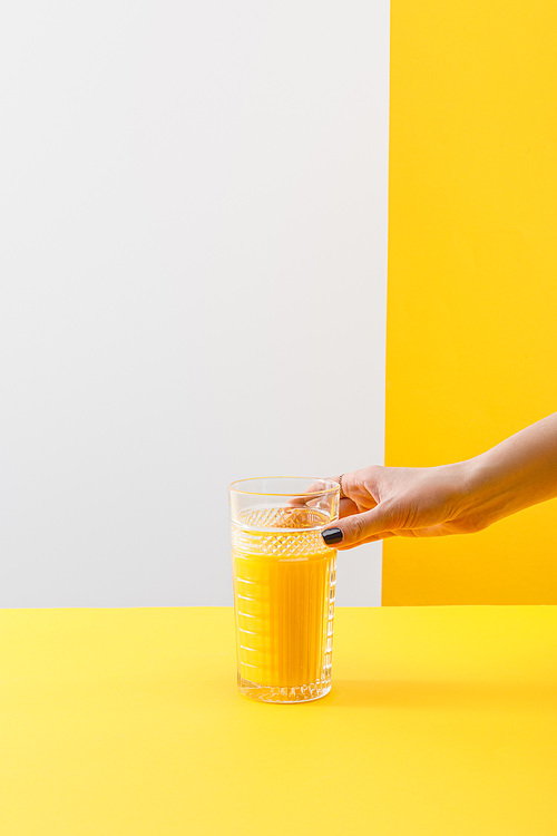 cropped view of woman holding glass of fresh delicious yellow smoothie on grey and yellow background