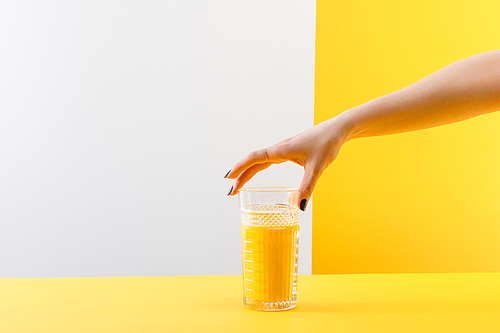 cropped view of woman holding glass of fresh delicious yellow smoothie on grey and yellow background