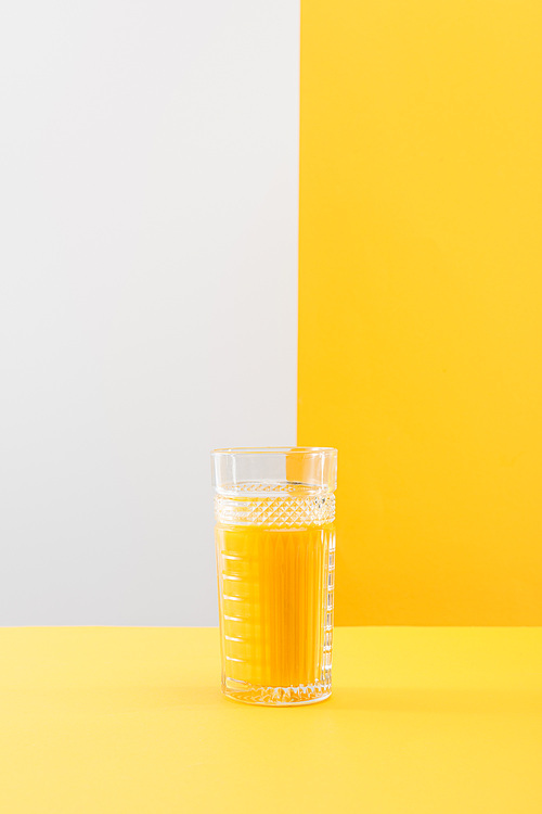 glass of fresh delicious yellow smoothie on grey and yellow background
