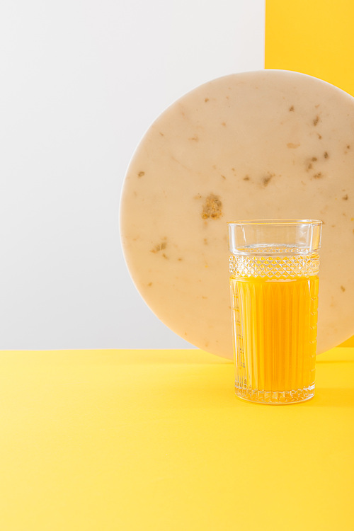 glass of fresh delicious yellow smoothie near marble circle on grey and yellow background