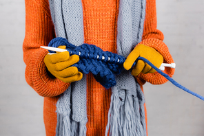 Cropped view of woman in gloves and sweater knitting on white background