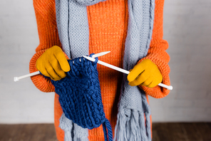 Cropped view of woman in warm sweater and gloves knitting with wool thread