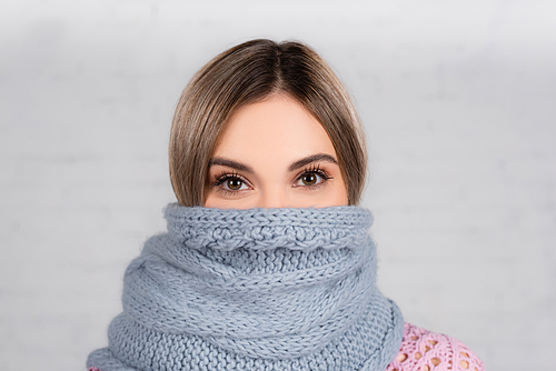 Young woman wrapped in knitted scarf  on grey background