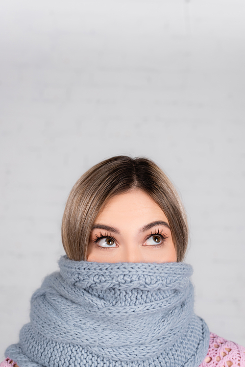 Woman wrapped in knitted scarf looking up on white background
