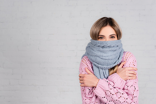 Woman in warm scarf and sweater suffering from cold on white background
