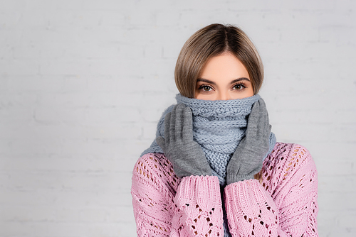Woman in knitted sweater and gloves wrapped in scarf  on white background