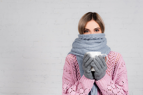 Woman in warm sweater, scarf and gloves holding cup on white background