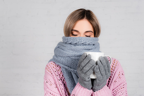 Young woman wrapped in warm scarf holding cup on white background